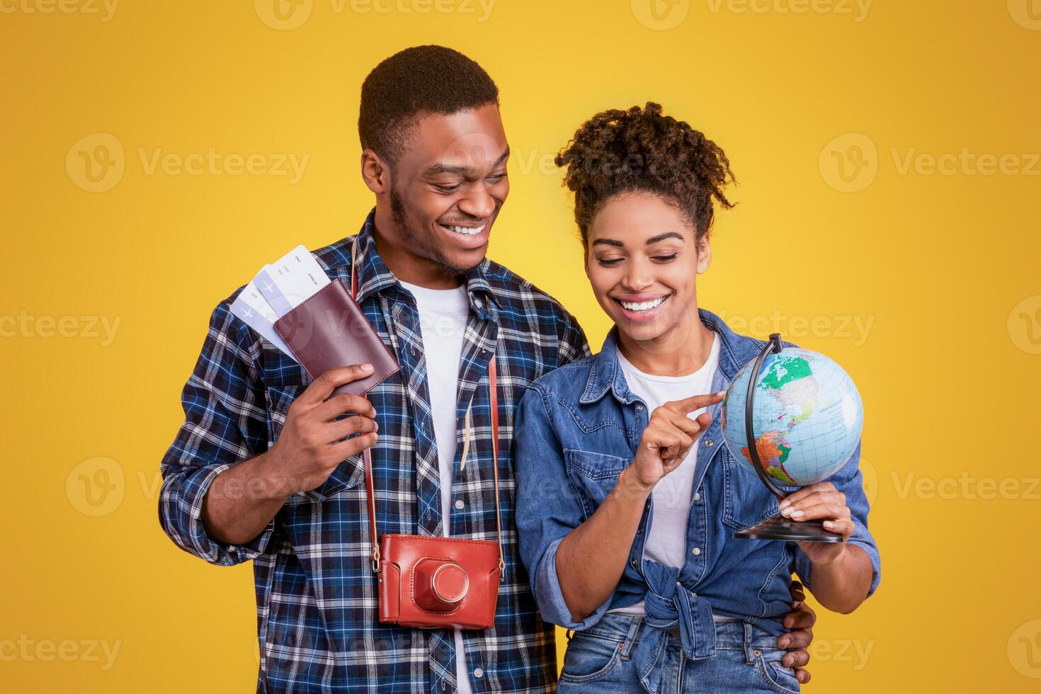 Cheerful African American Couple Of Tourists Holding Globe And Tickets Choosing Travel Destination For Vacation Standing On Yellow Background In Studio. Travelers Navigation, Traveling And Tourism photo