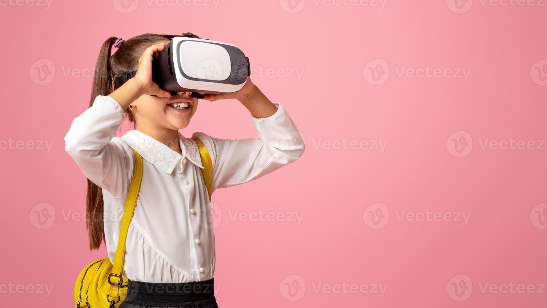Technology of future. Little schoolgirl enjoys virtual reality glasses, isolated on pink background photo
