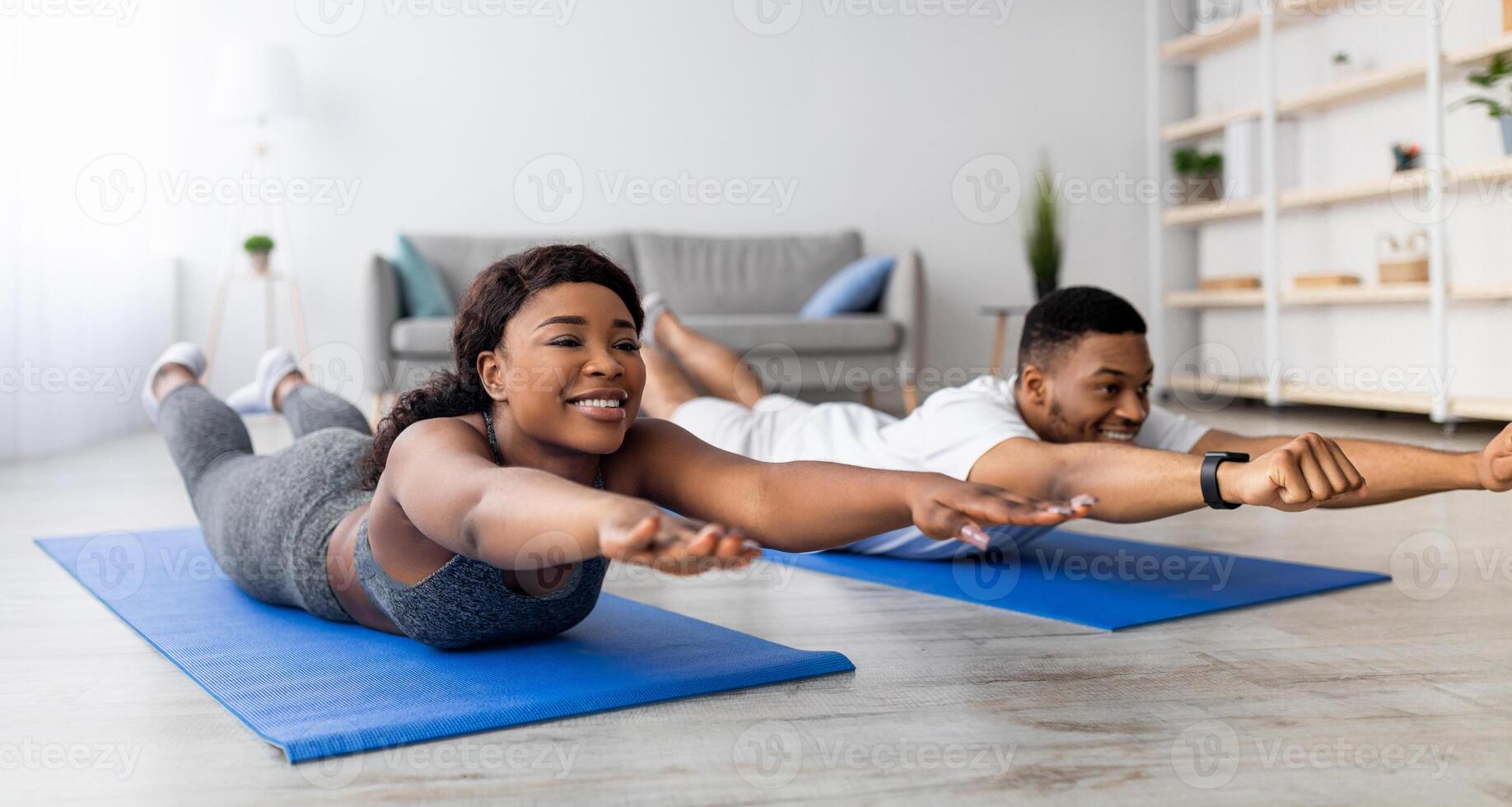 Home trainings during covid lockdown. Strong black couple exercising on sports mats, doing yoga or pilates indoors, panorama. Athletic African American family leading active lifestyle photo