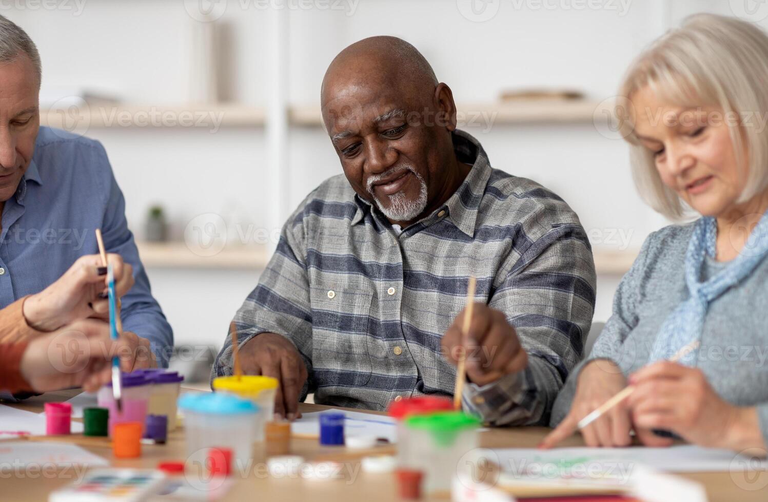Art therapy for seniors concept. Happy multiracial elderly men and women enjoying painting with brush, having conversation and smiling, attending drawing master-class together photo