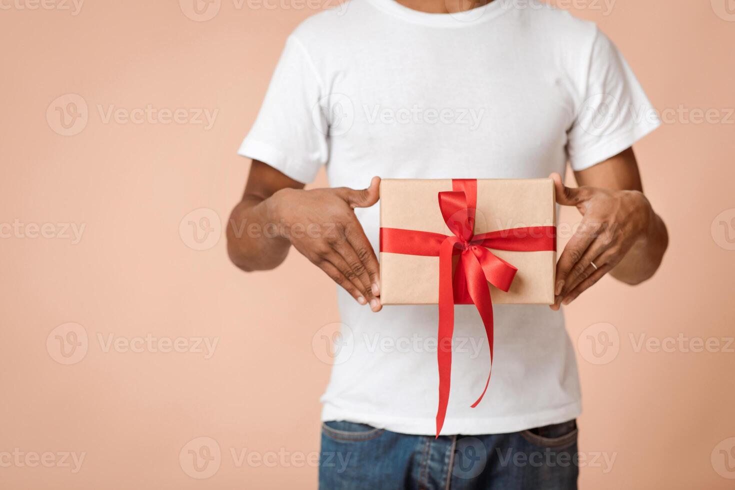 Surprise for Christmas, New Year and family party. African american man in white t-shirt holding box with gift in package with ribbon isolated on light background, cropped, studio shot, free space photo