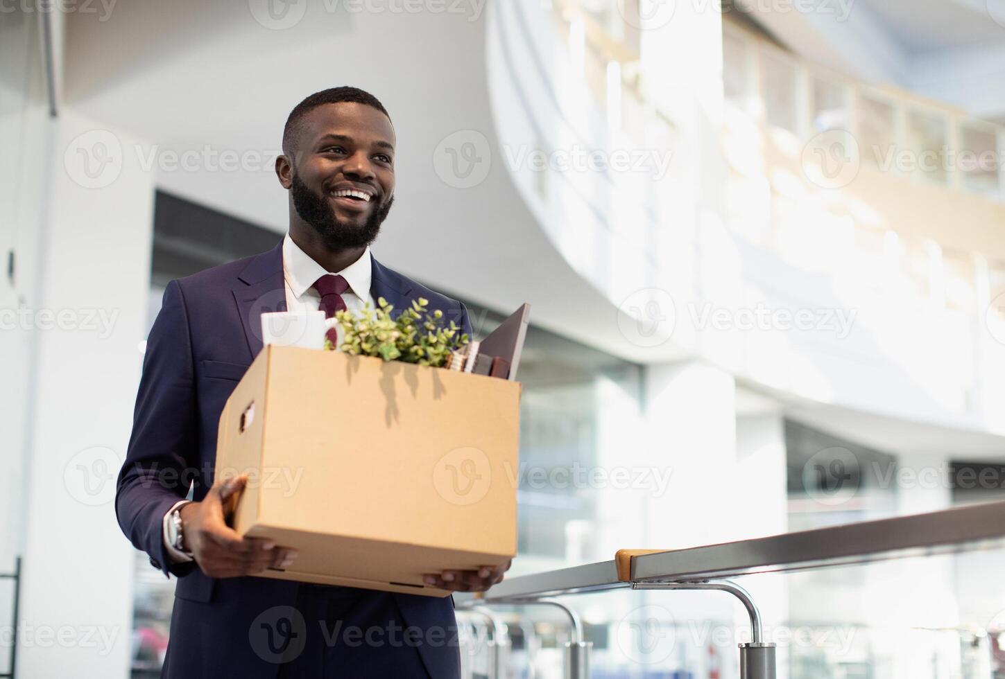 Happy young black man in suit got new job, walking by modern office, holding box with his belongings, looking at copy space and smiling. Job opportunity, career for millennials concept photo