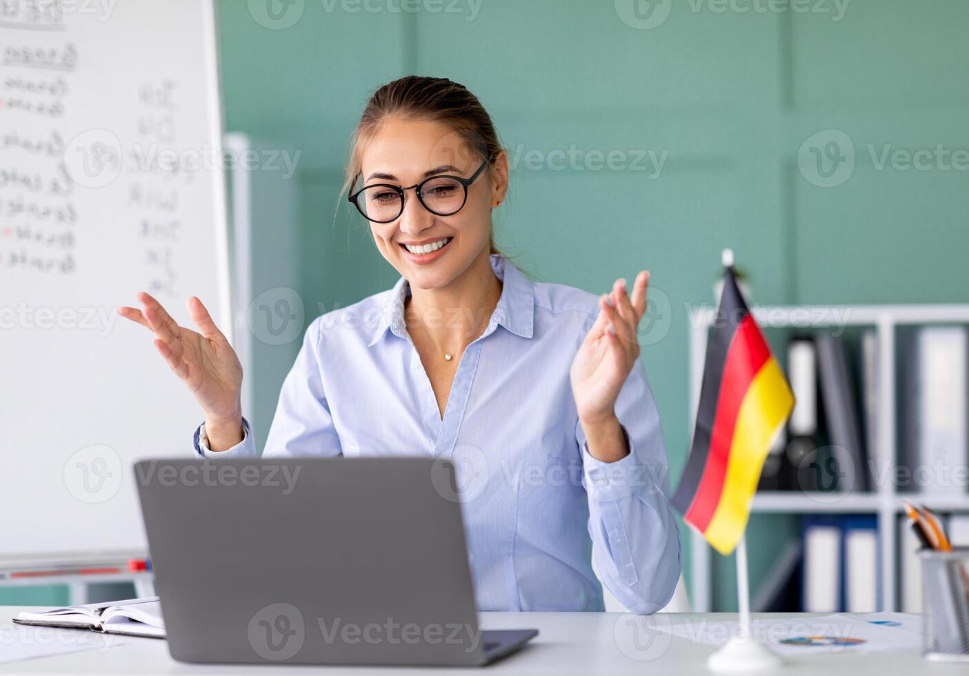 E-learning with teacher, social distancing, new normal. Happy female tutor giving German language lesson online, using laptop. Young lecturer explaining grammar rules to students on internet photo