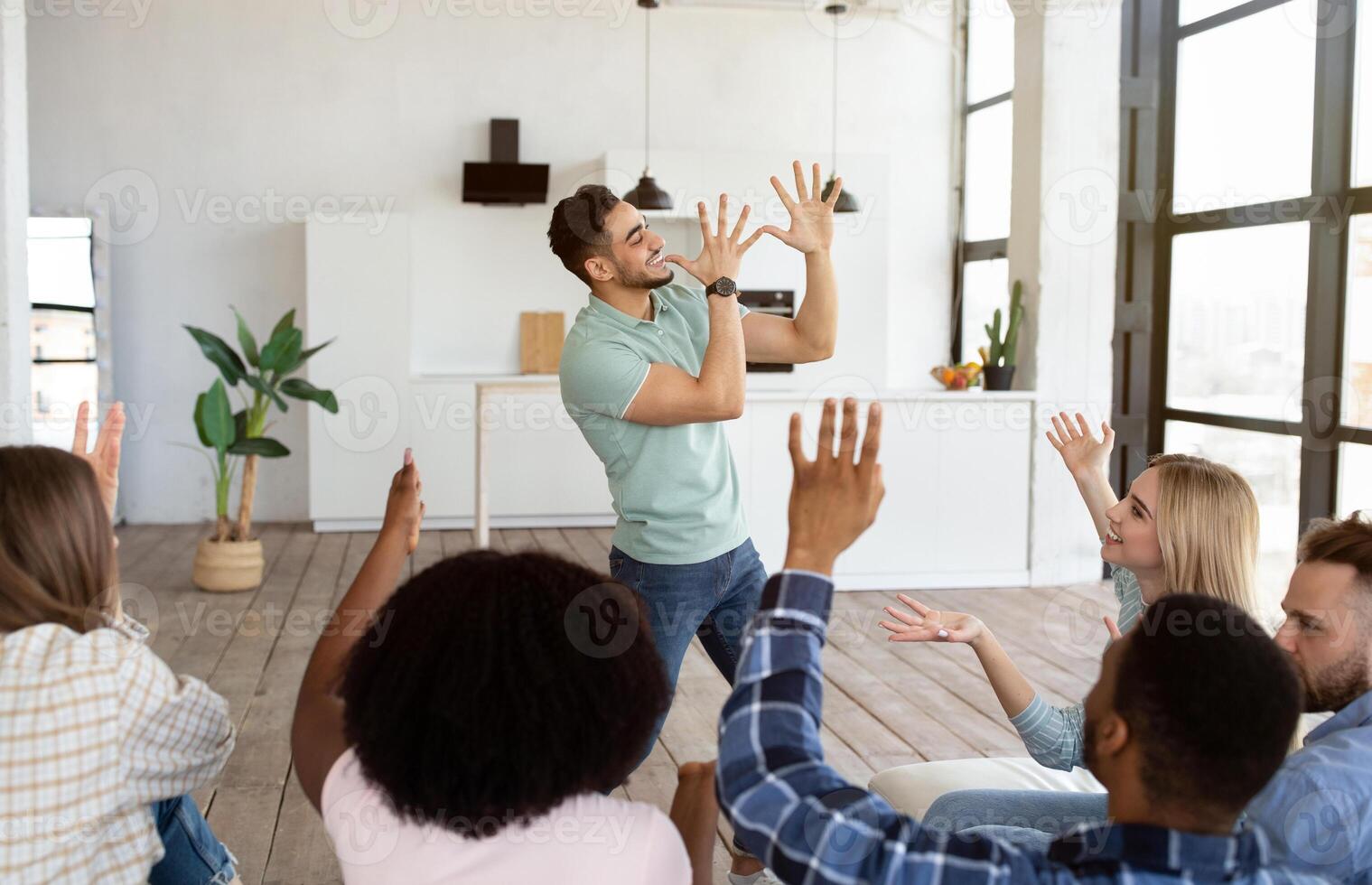 Young multiracial friends playing charades game at home. Arab guy showing pantomime riddles, his fellow students trying to guess during student party. Fun domestic entertainments concept photo
