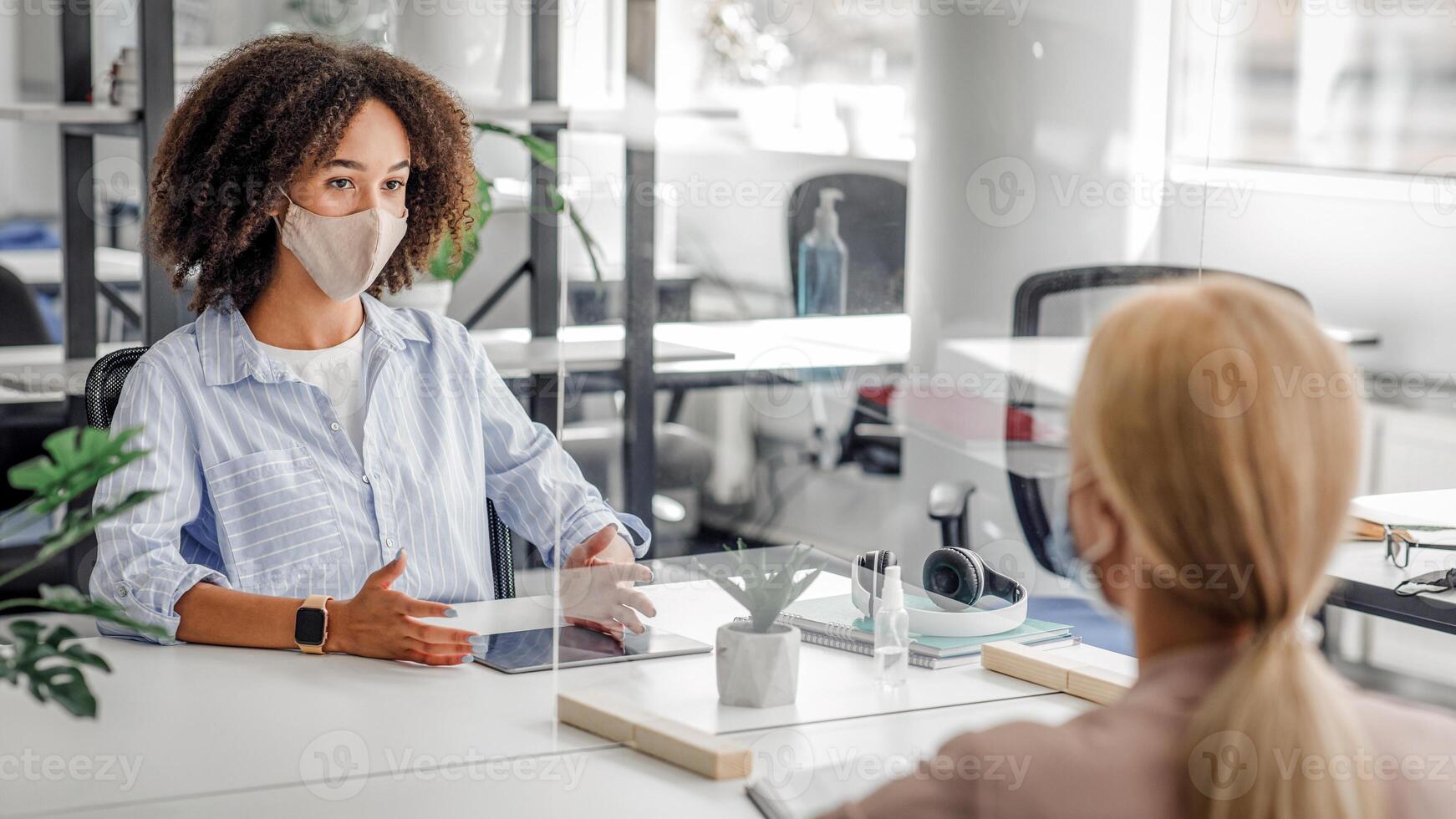 Interview. Young business workers from different ethnicities in protective mask talking to each other in office through partition to prevent COVID-19 infection photo
