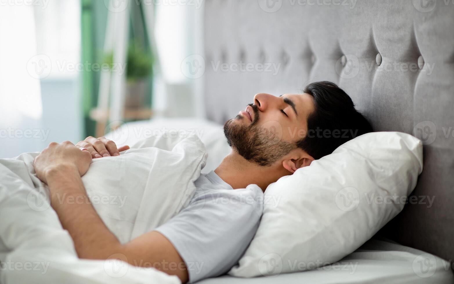 Deep male sleep. Young arab guy sleeping peacefully in his comfortable bed at home, lying with closed eyes on back. Recreation, time to rest and nap concept photo