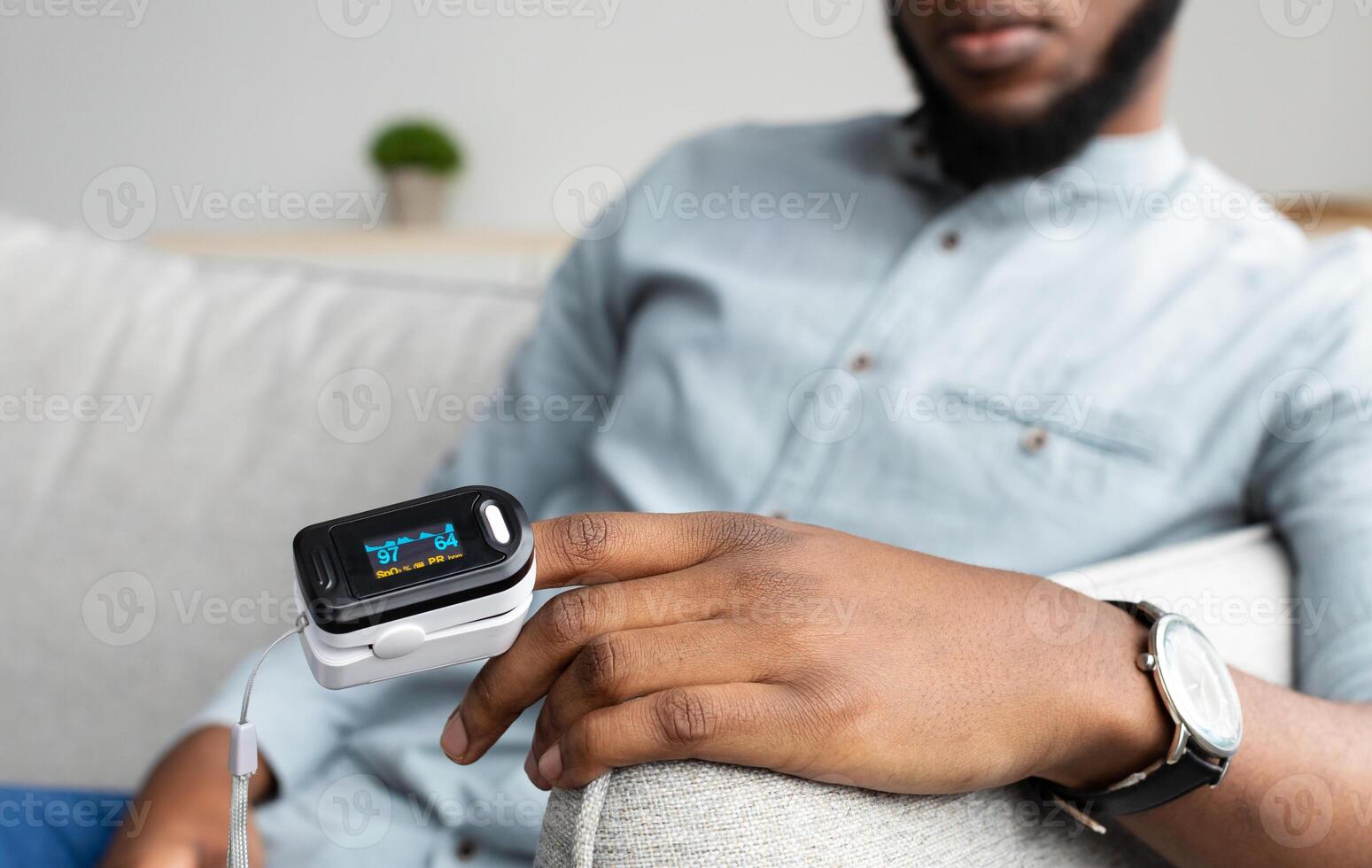 Unrecognizable Black Man With Pulse Oximeter On Hand Measuring Oxygen Saturation Level At Home. Pulseoxymeter Medical Device, Pulseoxymetry Clip Machine Monitorin Ox Rate. Cropped, Selective Focus photo