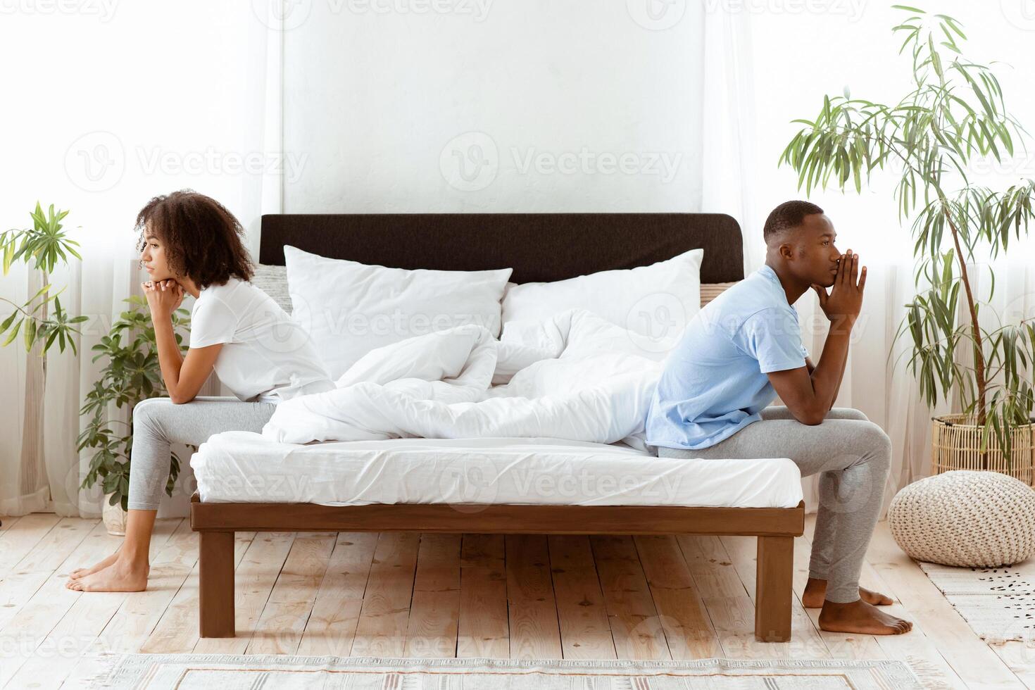 Couple ignoring each other in bed after quarrel. Upset millennial african american guy and woman sitting on different sides and turned away in modern bedroom interior in morning, profile, copy space photo