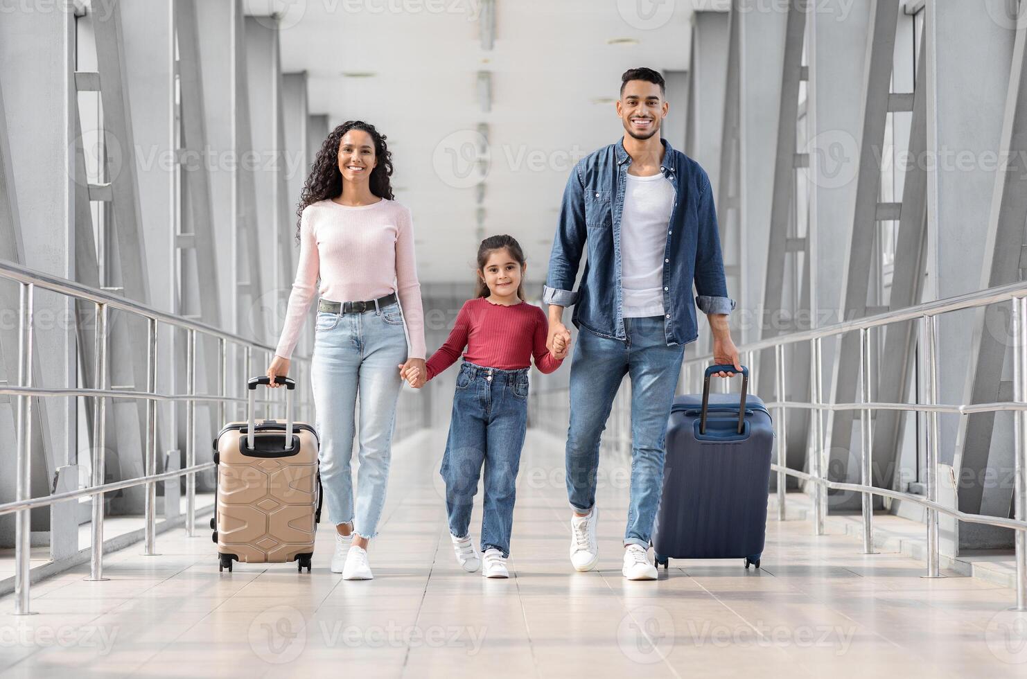 Ready For Vacation. Happy Middle Eastern Family Of Three Walking With Suitcases At Airport Terminal, Smiling Arab Parents With Little Daughter Holding Hands, Enjoying Travelling Together, Copy Space photo