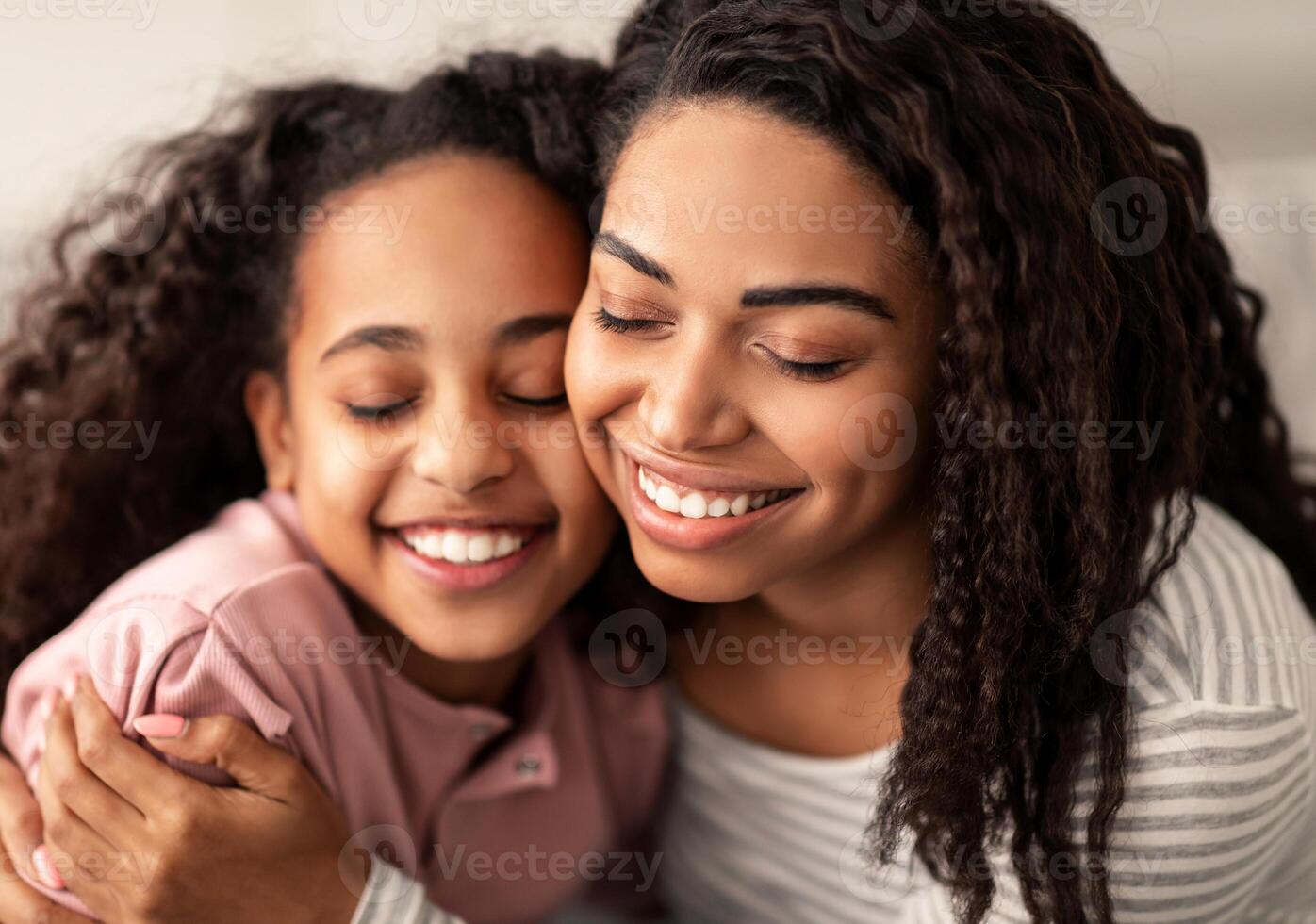 Bonding And Togetherness Concept. Close up portrait of African American mom and daughter hugging and smiling, celebrating mother's day, enjoying time together. Happy woman cuddling with girl photo