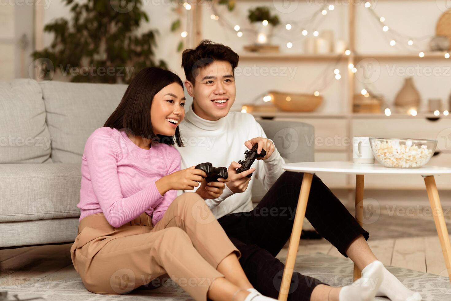 Chinese Girlfriend And Boyfriend Playing Videogame Using Games Console Sitting On Floor At Home. Computer Gaming And Videogames For Couple, Family Weekend Leisure Concept photo