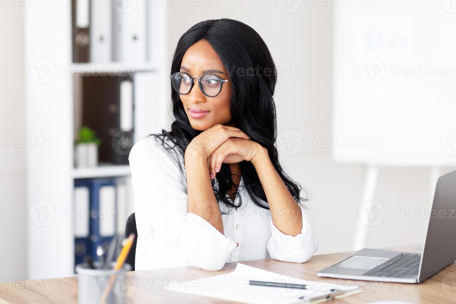 Portrait of young female secretary daydreaming in front of laptop at workplace, copy space. Millennial black business lady taking break from online work, looking aside at her table in office photo