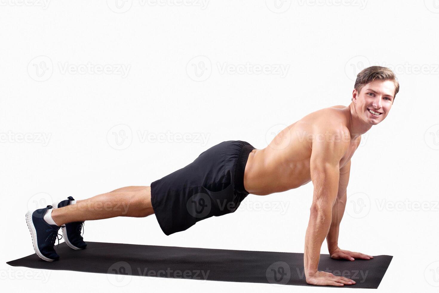 Smiling millennial sportsman standing in plank pose or doing push ups over light studio background, blank space. Happy young athlete with sexy body exercising on yoga mat, panorama photo