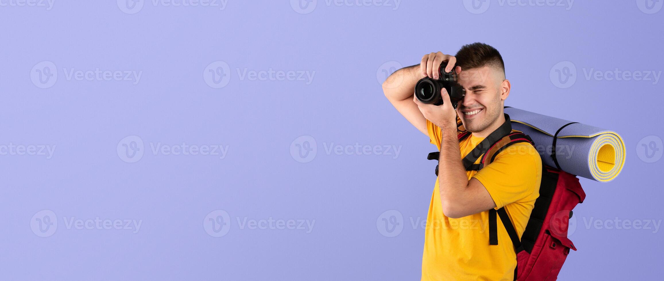 Cheerful young traveler with backpack and camera ready to take photos on blue background