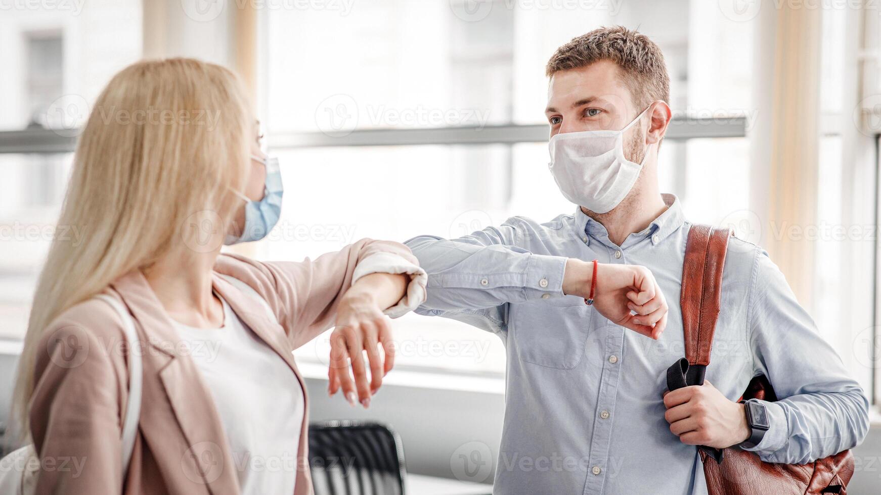 Say hello and greet, social distance and return to work after quarantine. Millennial man and woman in protective masks are touched by elbows in office during COVID-19 epidemic, free space photo
