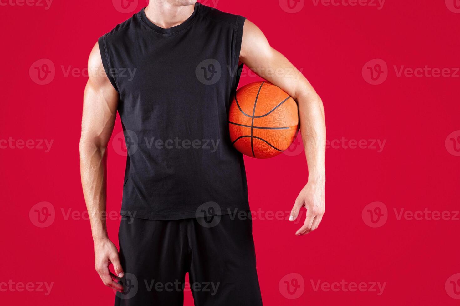 Cropped view of young basketball player holding ball on red studio background, copy space. Millennial athlete in sportswear ready for streetball tournament, close up of hands photo
