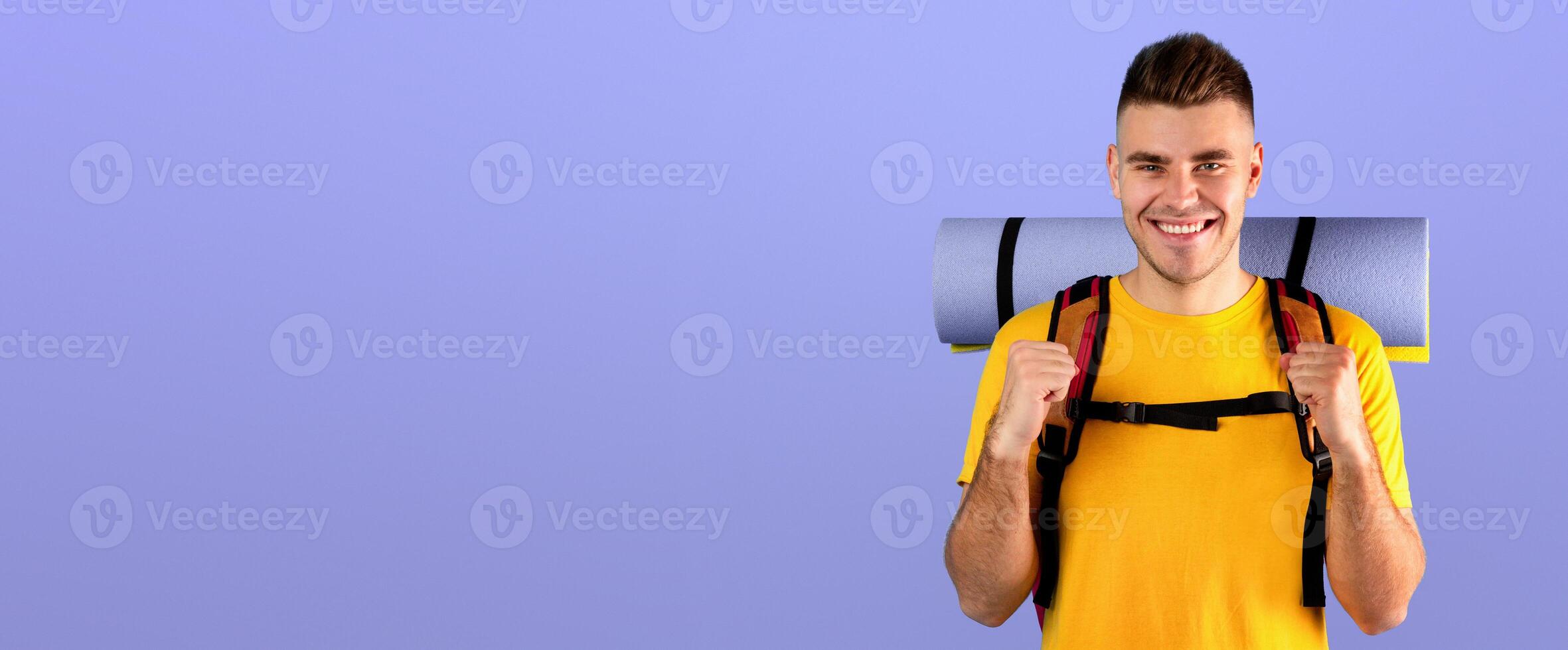 Cheerful young guy with tourist gears gesturing YES over blue studio background. Positive millennial hiker thrilled about his journey, anticipating camping trip or adventure photo