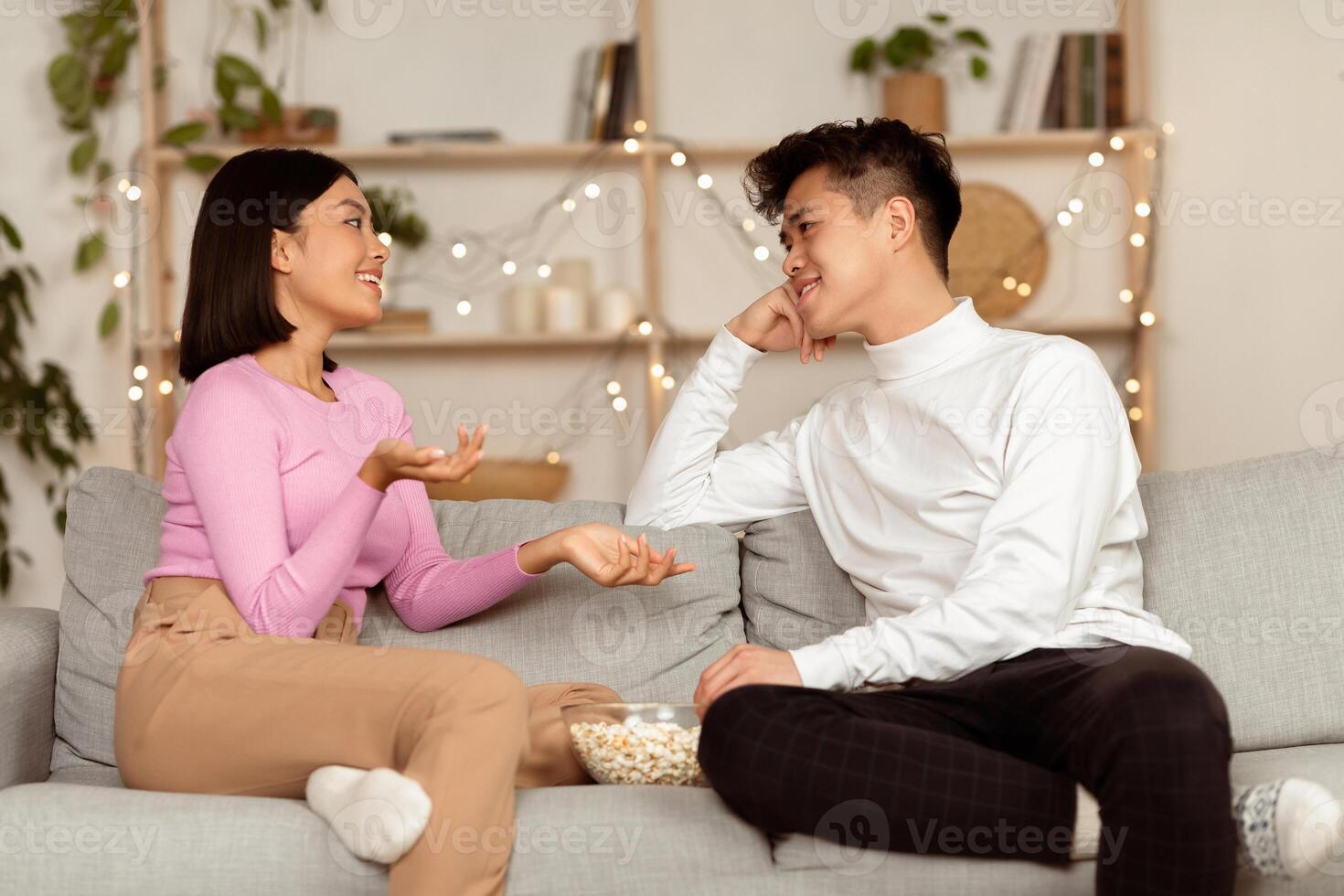 Dating Asian Couple Having Stay-At-Home Date, Flirting And Talking On Different Topics Eating Popcorn Sitting On Couch At Home. Weekend Evening Together photo