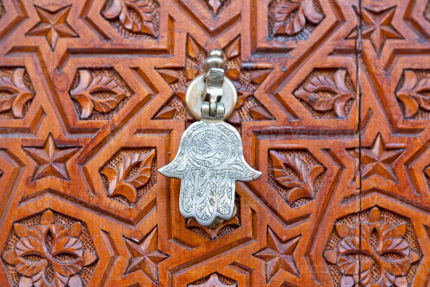 Hamsa shaped door knocker on an old carved wooden door photo