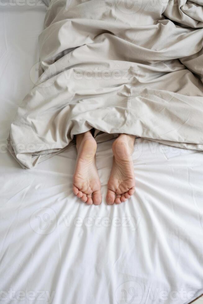 Bare Feet Of A Relaxed Person Protruding From Soft Beige Blanket On A Crisp White Bed photo