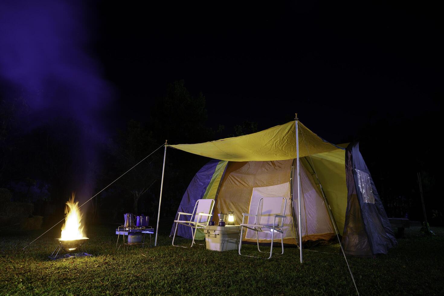 Camping tent on green grass at night, antique gas lamps, retro chairs, with outdoor coffee-making facilities on tables in a forest camping area in the forest photo