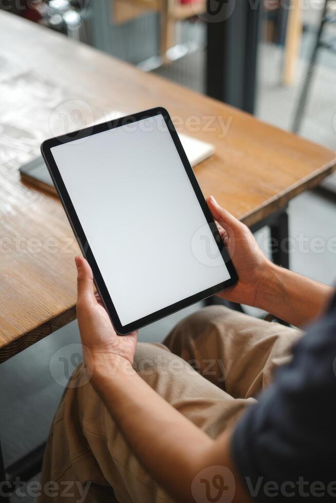 Person Holding Blank Digital Tablet In Cozy Workspace With Wooden Table And Soft Natural Light photo