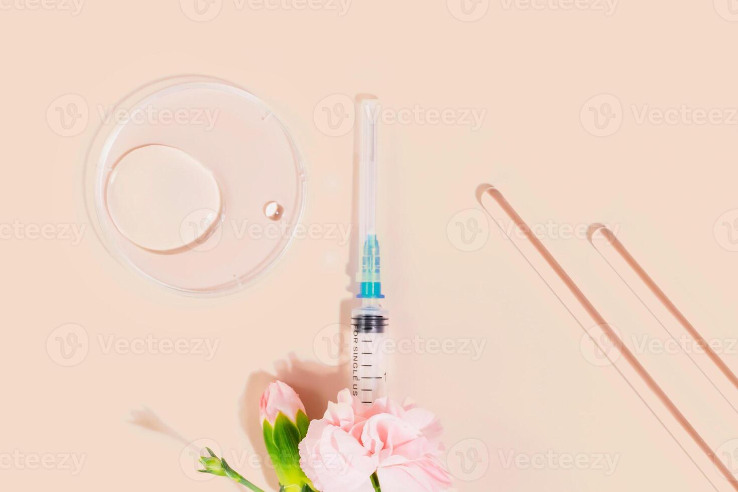 Syringe with pink flowers, lab tools, and petri dish on nude background photo