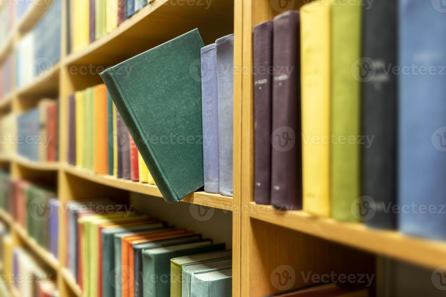 Green book extended from colourful books on shelves in public library photo