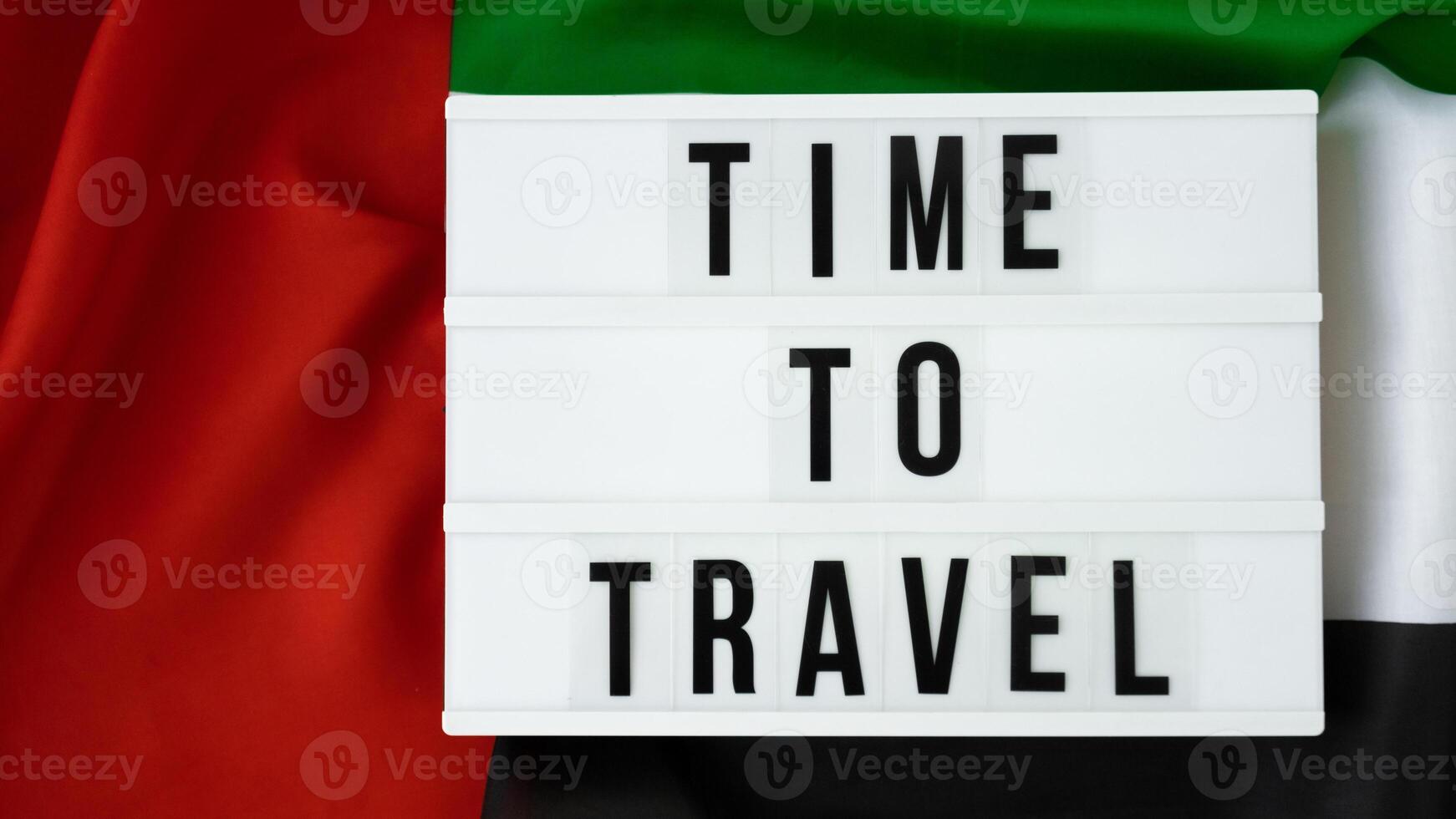 Lightbox with text TIME TO TRAVEL on background of waving UAE flag made from silk. United Arab Emirates flag with concept of tourism and traveling. Inviting greeting card, advertisement. Dubai welcoming card photo