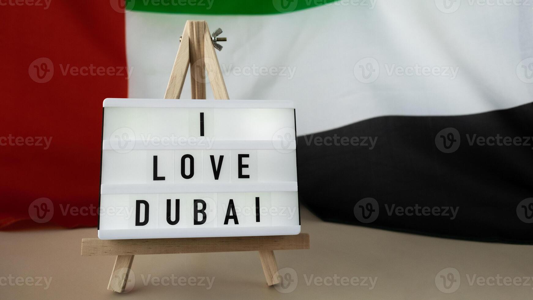 Message text I LOVE DUBAI on background of waving UAE flag made from silk. United Arab Emirates flag with concept of tourism and traveling. Inviting greeting card, advertisement. Dubai welcoming card photo