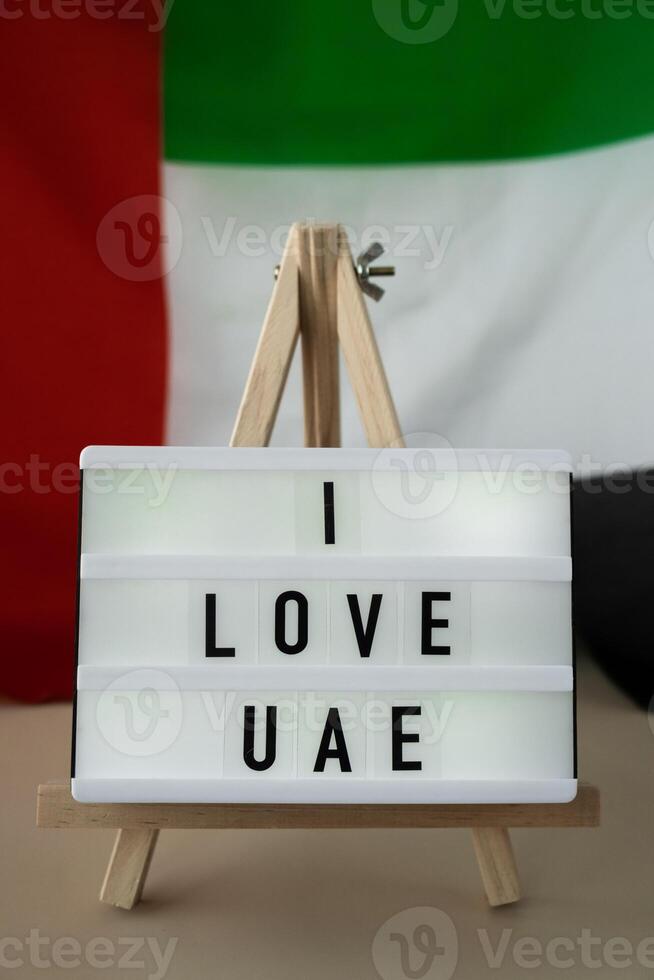 Lightbox with text I LOVE UAE on background of waving UAE flag made from silk. United Arab Emirates flag with concept of tourism and traveling. Inviting greeting card, advertisement. Dubai welcoming card photo