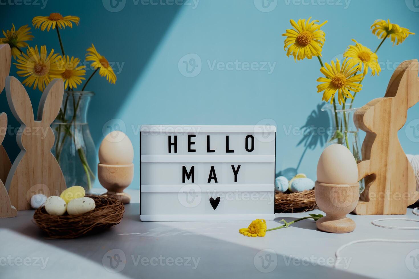 Lightbox with message HELLO MAY on festive blue background and eco-friendly zero waste natural decoration. Yellow daisies flowers. Bunny egg. Holiday greeting card photo
