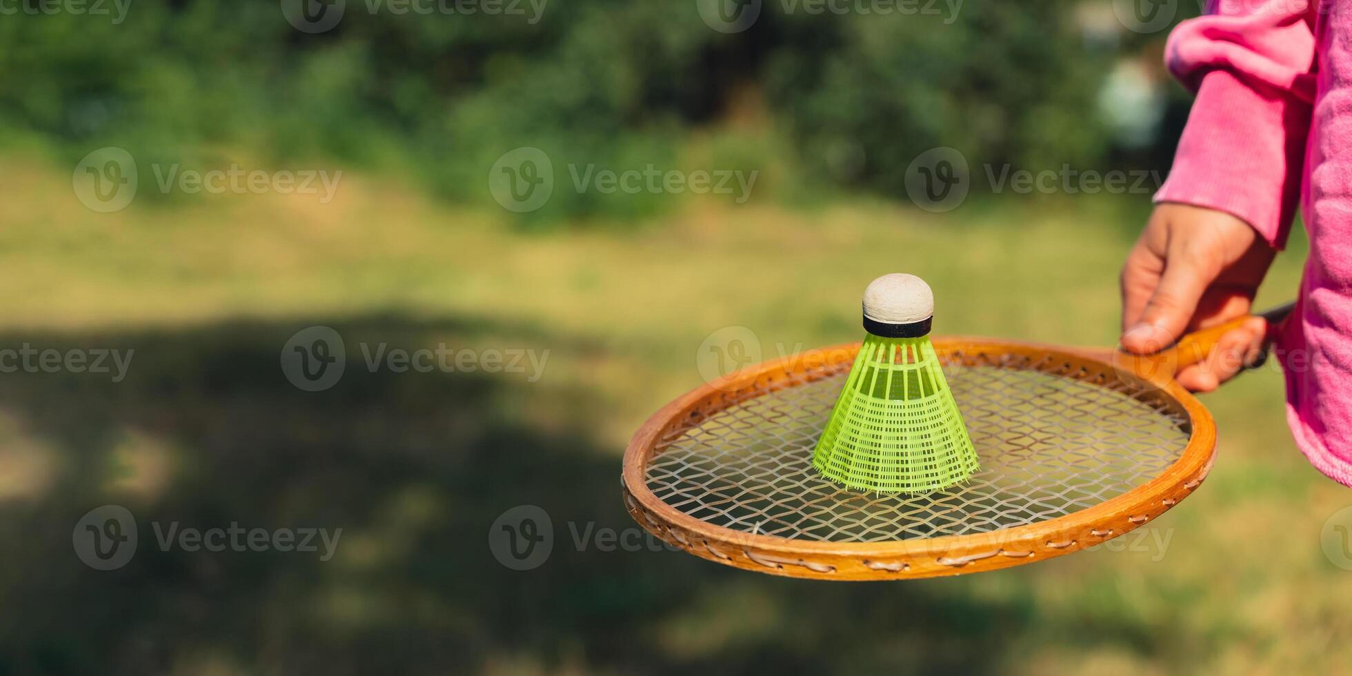 Female hand holding Neon yellow badminton shuttlecock and wooden racket outdoors. Copy space soft selective focus on shuttlecocks. Alternative fitness recreational sport photo