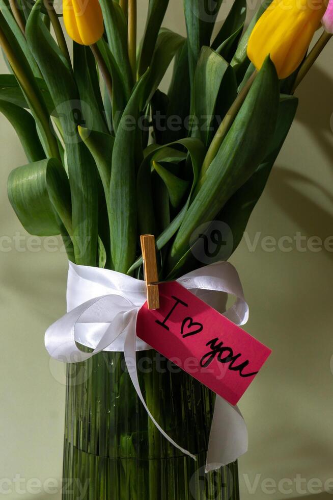 I LOVE YOU paper card Bouquet of colorful tulips in vase in pastel green background. Copy space for greeting card. Holiday flowers springtime atmosphere photo