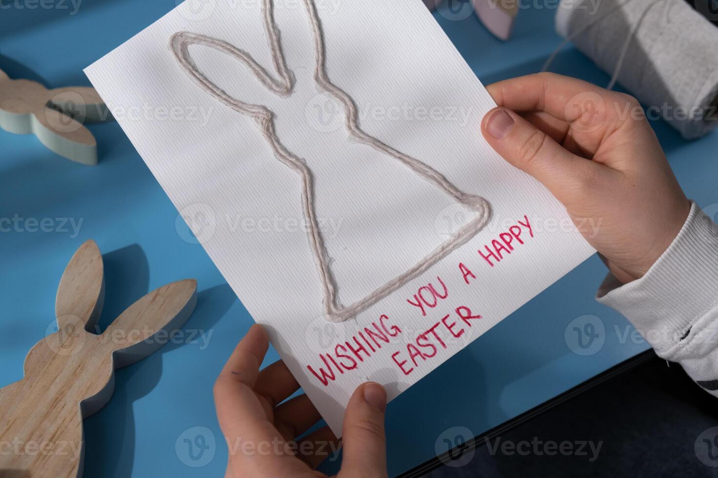 Person holding handmade greeting card with message WISHING YOU HAPPY EASTER written in beautiful handwriting. Gesture shows excitement and joy for the upcoming event. Springtime holiday gift present zero cost ideas. Creative art preparation photo
