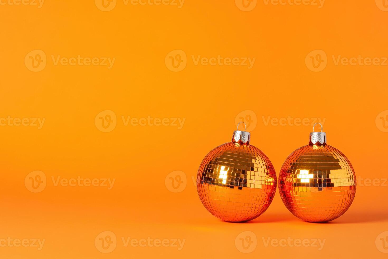 Two shiny orange disco ball christmas ornaments sit on an orange background, creating a festive and vibrant scene photo