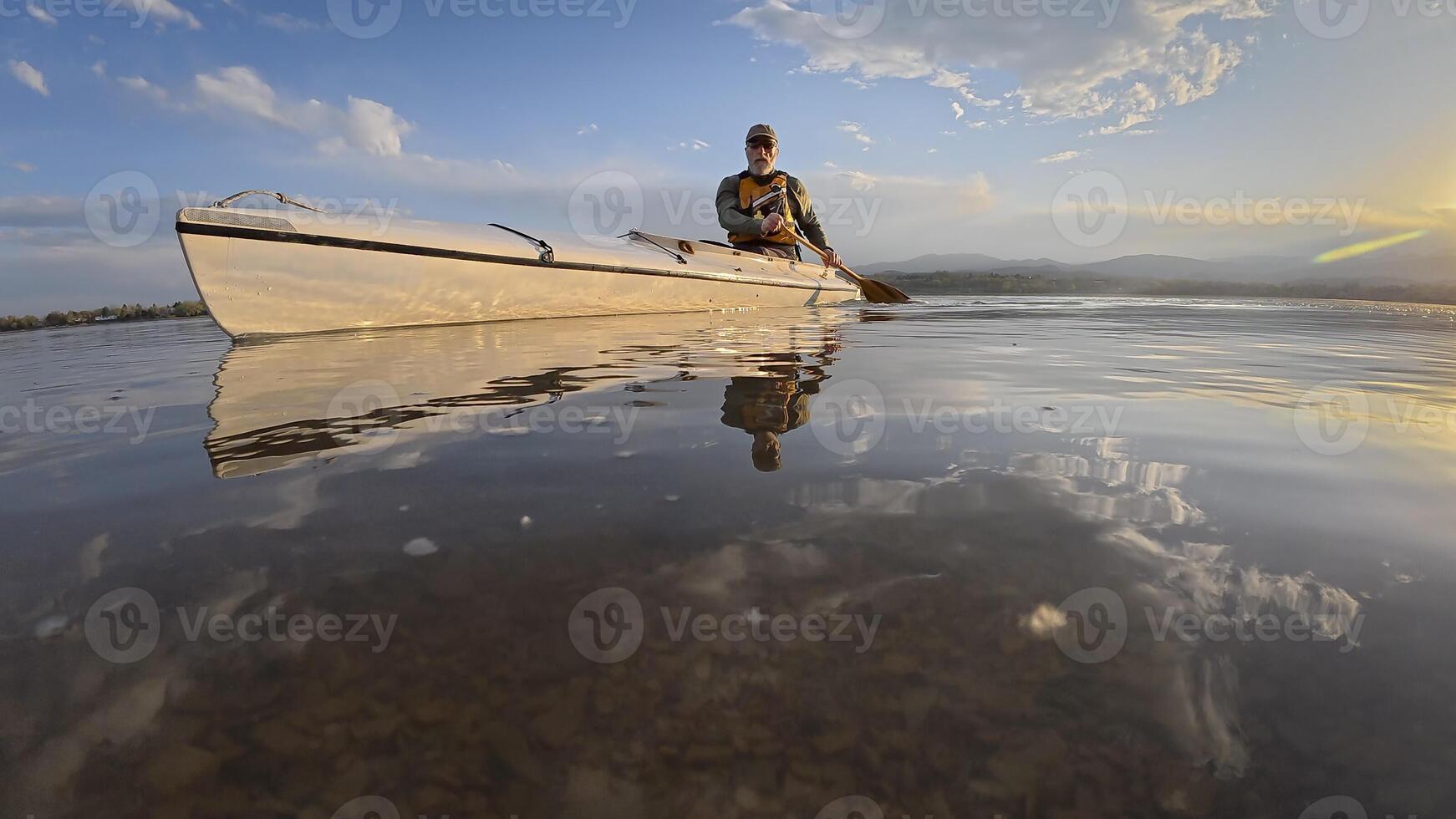 low angle view of a senior canoe paddler on a calm lake at sunset photo