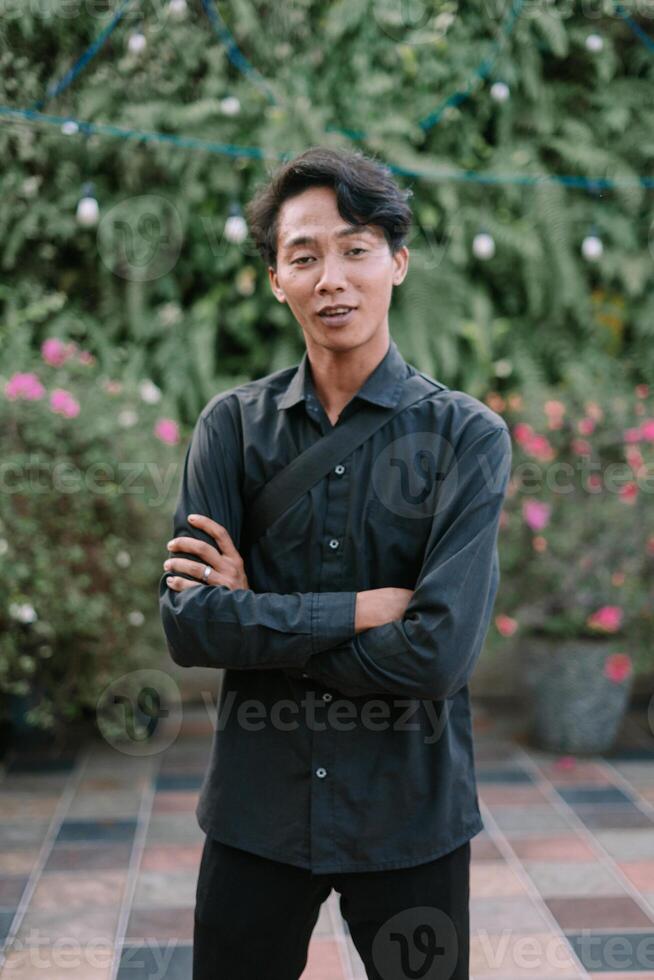 Contemplative young man in garden setting with arms crossed casually photo