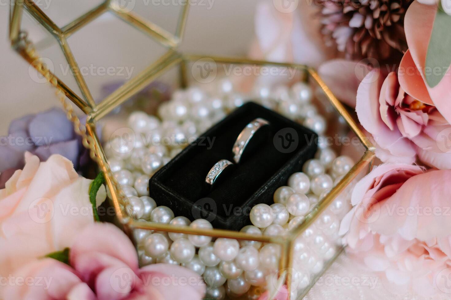 Elegant wedding rings in geometric glass box with pearl beads and flowers photo