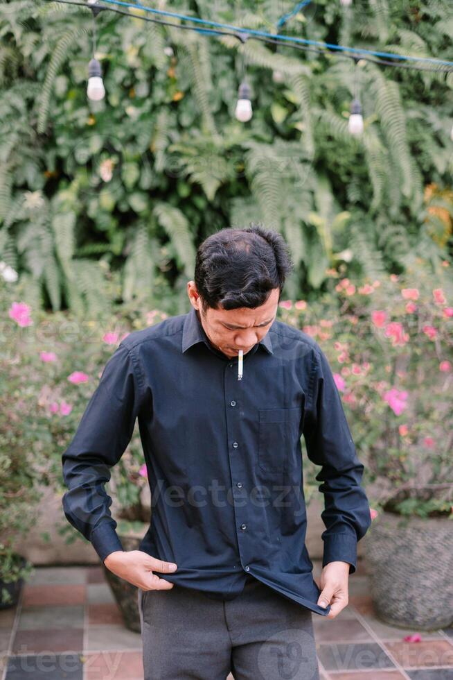 Pensive man with cigarette standing outdoor amidst lush greenery photo