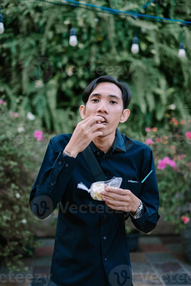 Man in a lush garden snacking on a treat while wearing a dark shirt photo