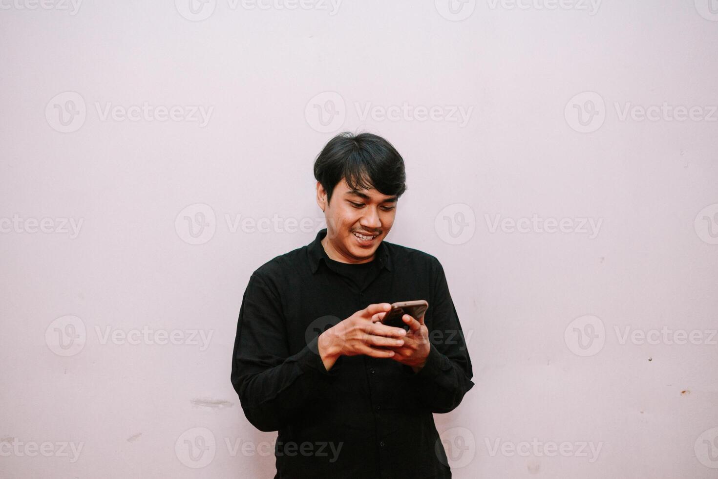 Contented asian man interacting with cellphone against light background photo