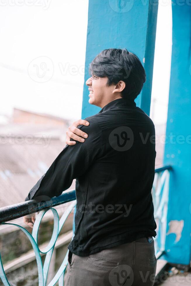 Thoughtful young man smiles on vintage balcony with blue railing photo