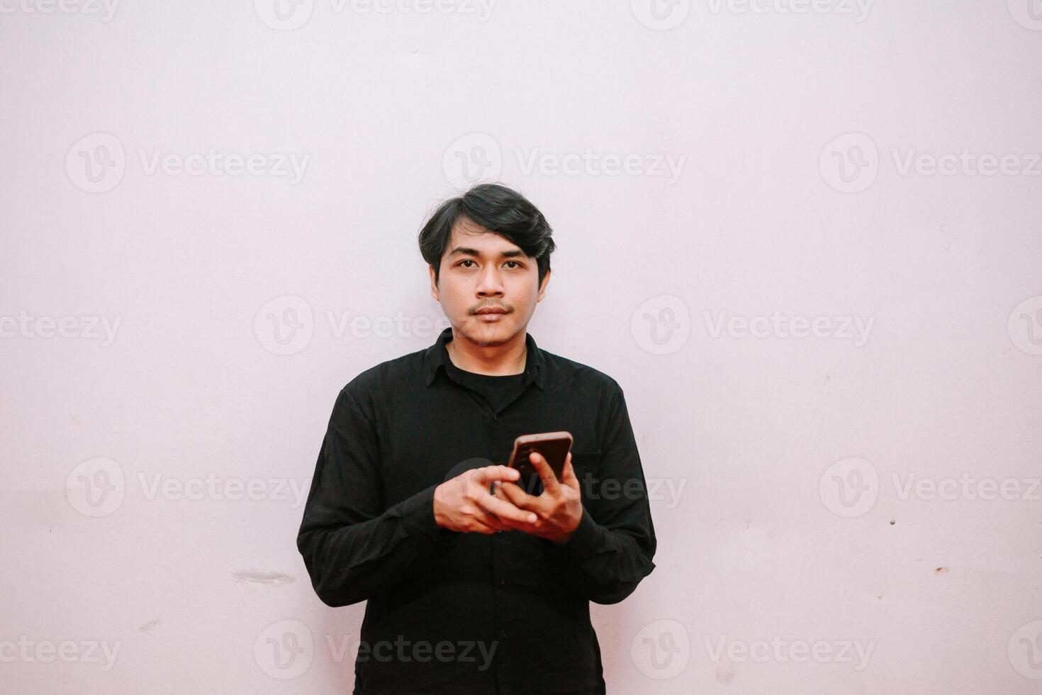 Man in Black Shirt Holding Smartphone Against Pink Wall Background photo