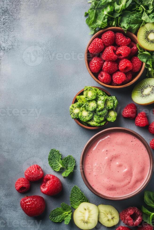 Overhead view of a fresh pink smoothie with raspberries kiwi spinach and mint leaves arranged on a textured gray surface photo