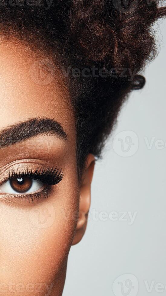 Close view of face. Single eye with long lashes and brown iris. Curly dark hair above. Neutral light background. Part of face. photo