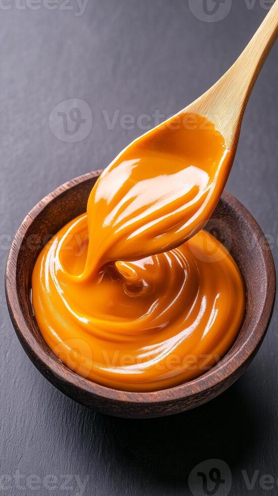 Rich and smooth caramel sauce is swirled in a wooden bowl, perfect for drizzling over ice cream, pastries, or as a dip for fruits photo