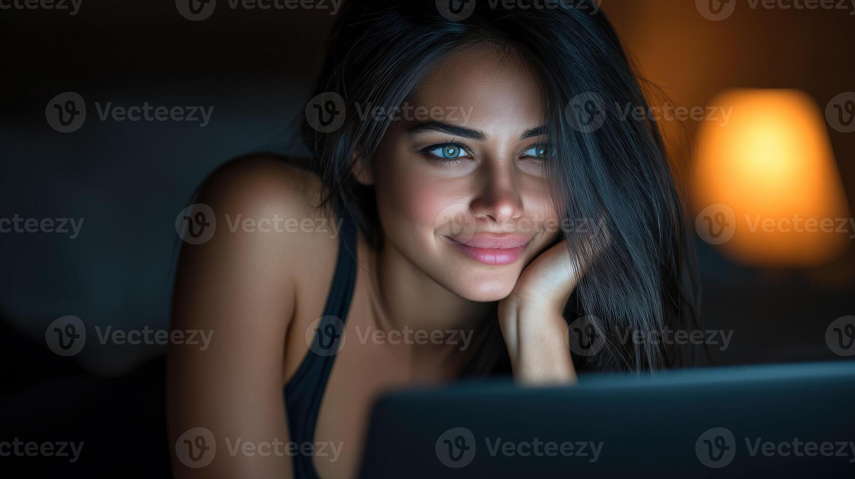 Smiling woman using laptop at night with warm light ambiance surrounding her photo