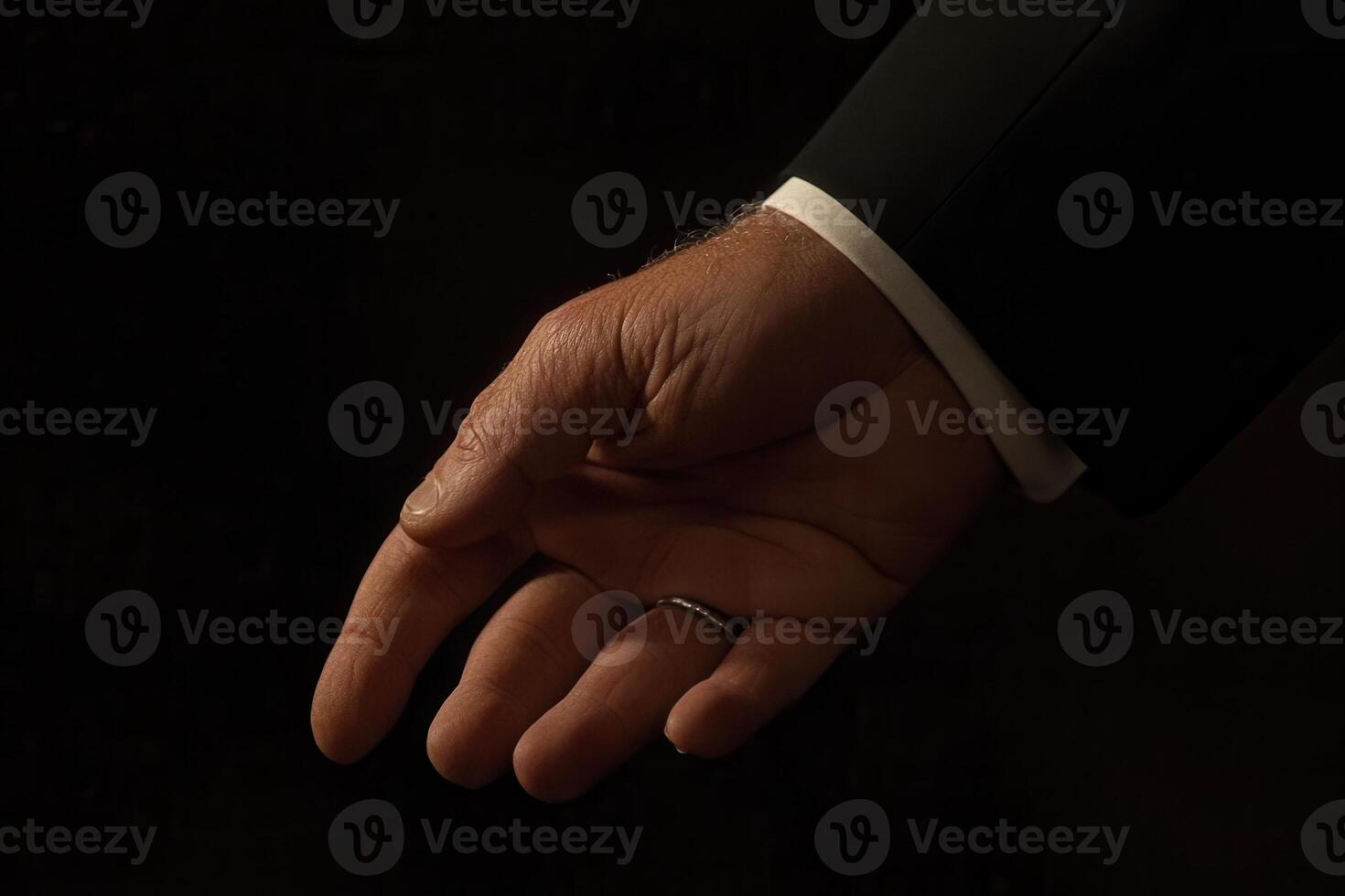 Elegant hand in formal attire reaching out against a dark background, conveying invitation photo