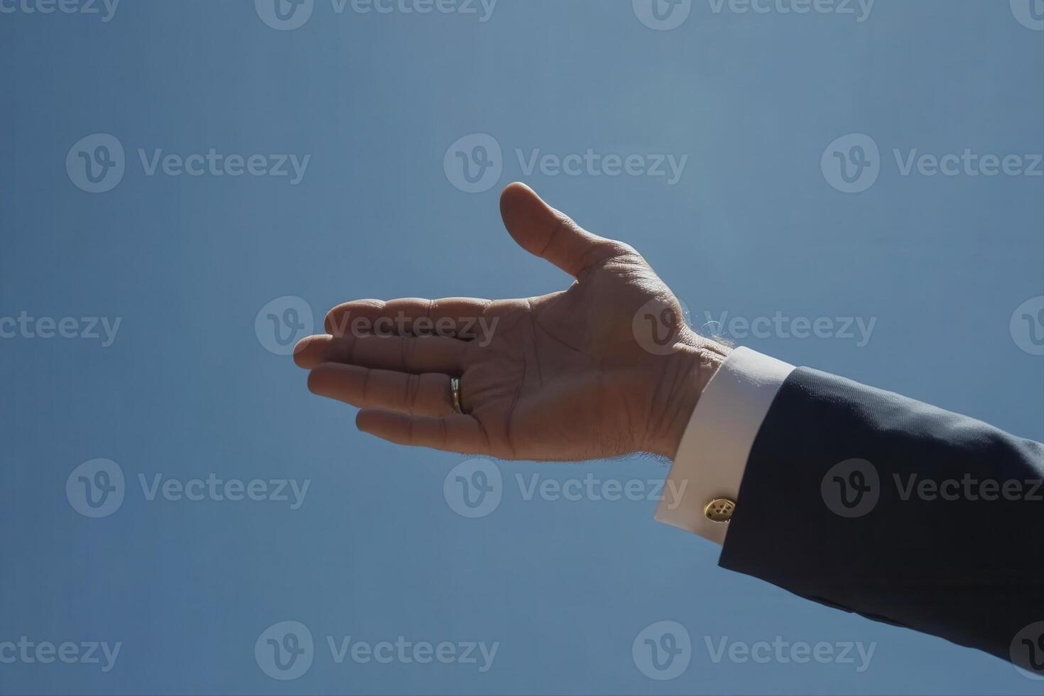 A business professional extending a hand against a clear blue sky, symbolizing greeting or collaboration photo